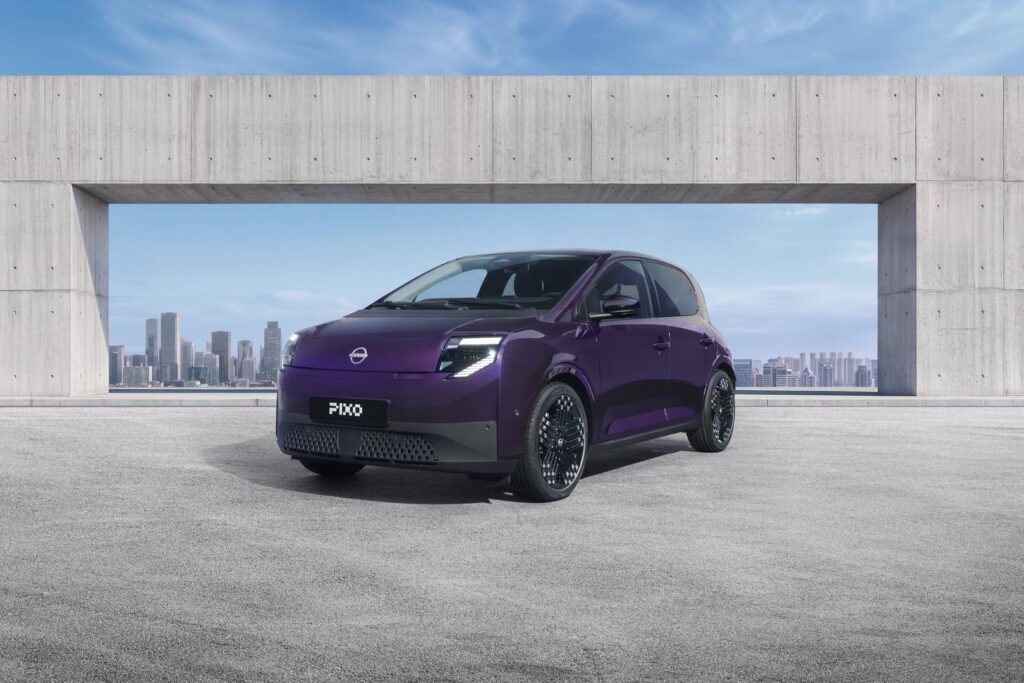 Three-quarter front view of a purple Nissan PIXO electric city car parked beneath a modern concrete structure, with a city skyline in the background.